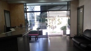 Zona de recepción con separador de vidrio, mostrador de recepción, sofá de cuero negro y un carrito.