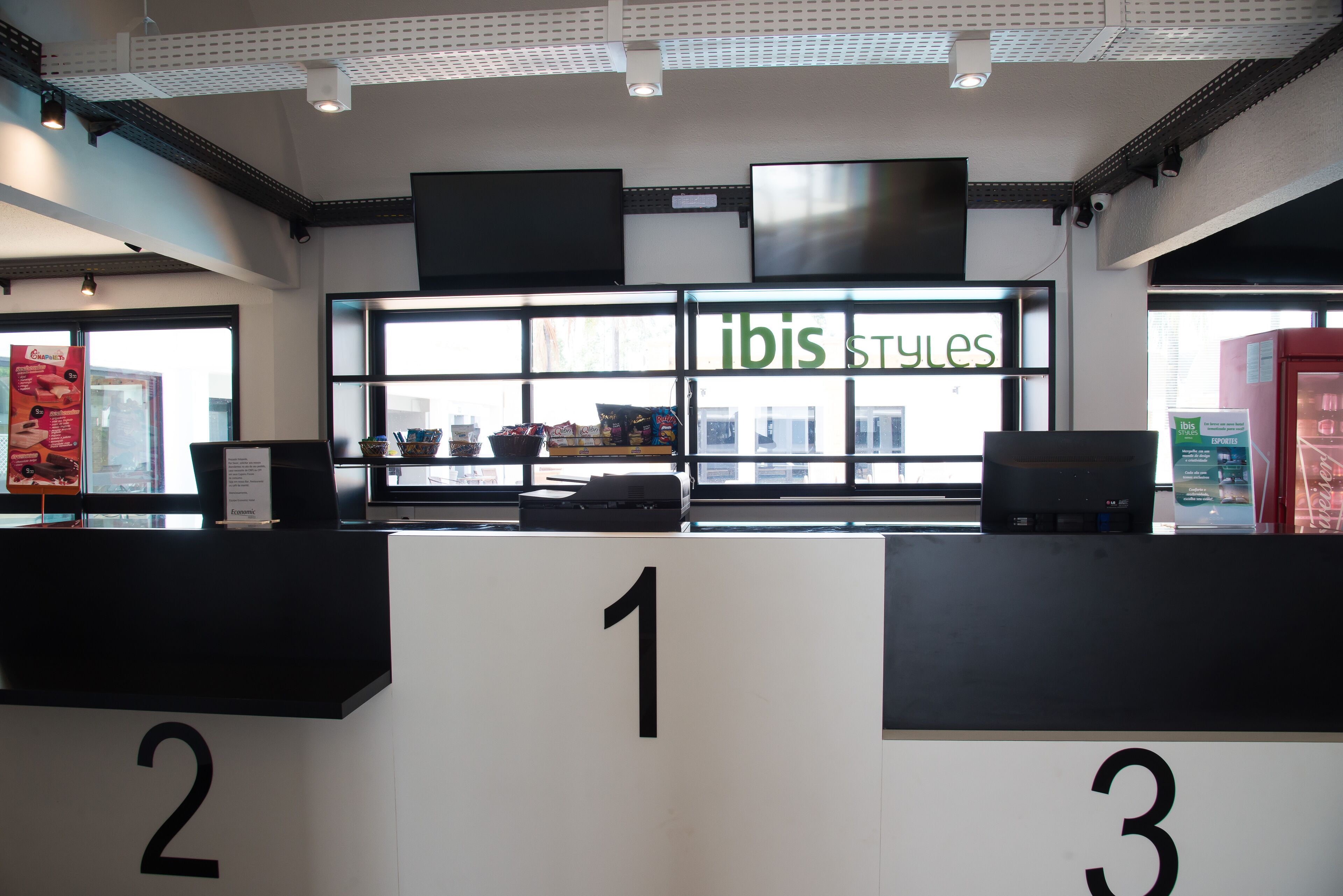 A reception area with numbered counters, a large window displaying 'ibis Styles', and a view of the outside.