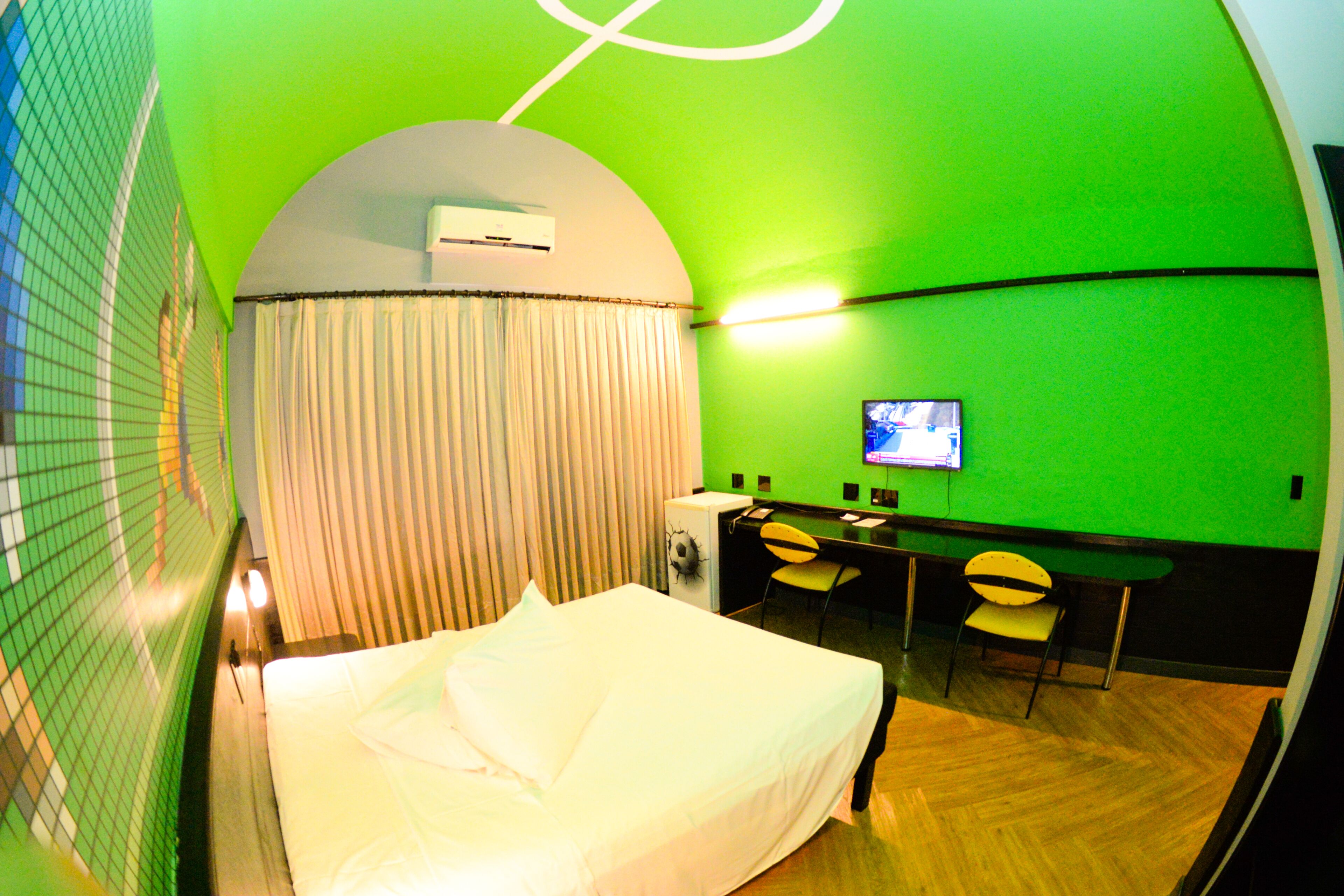 A hotel room with a bed, a desk with a chair, a television, and an air conditioning unit.