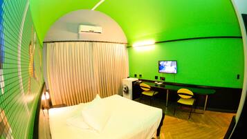 A hotel room with a bed, a desk with a chair, a television, and an air conditioning unit.