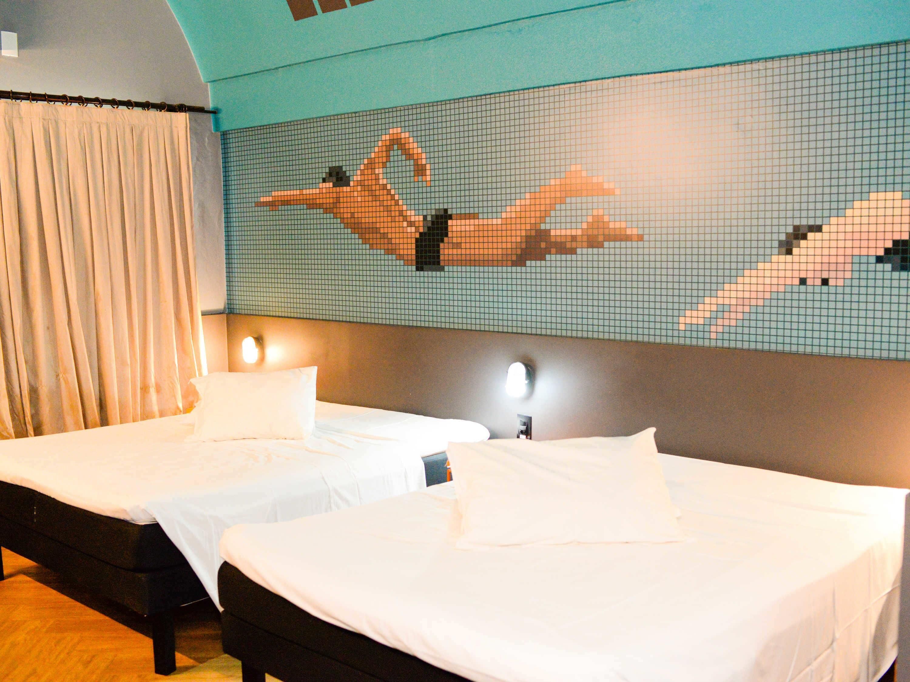 Quarto de hotel com duas camas, um mural de azulejos e uma cortina.