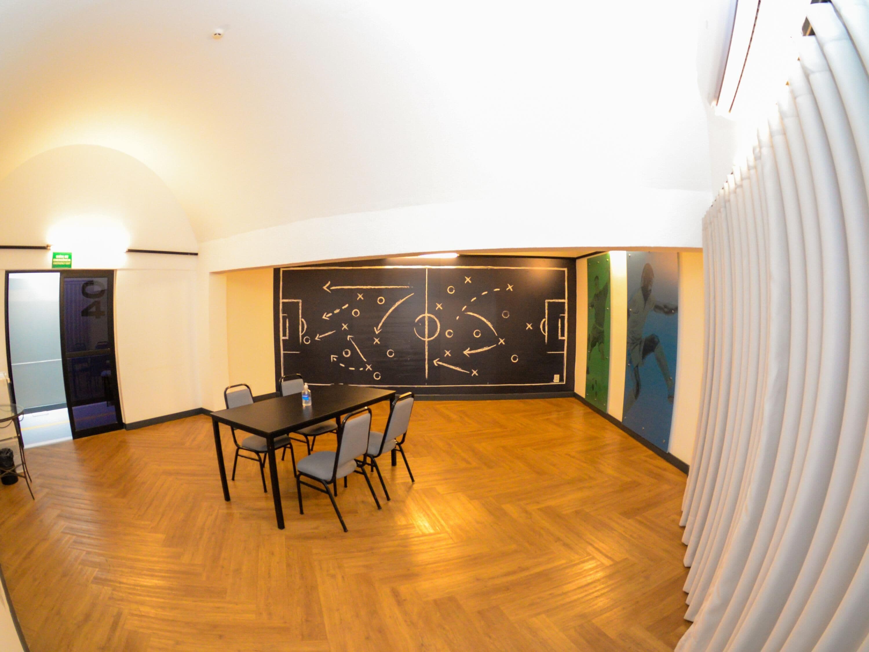 A conference room with a blackboard displaying a soccer field diagram, wooden flooring, and a table with chairs.