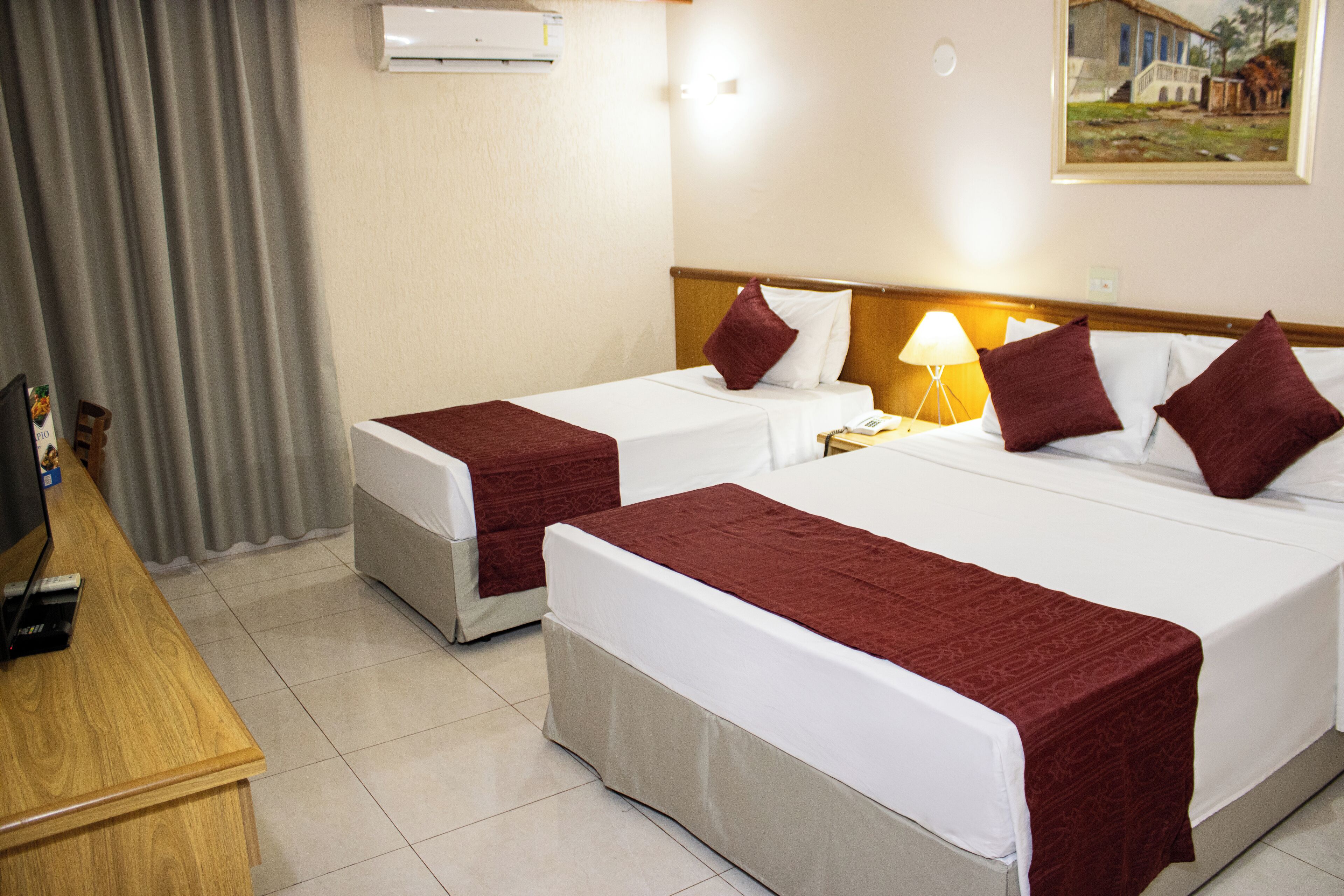 A hotel room with two beds, a desk, and a lamp.