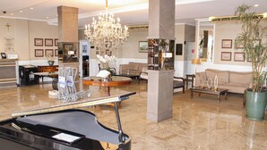 A lobby with a grand piano, a chandelier, a reception desk, and a seating area with a sofa and coffee table.