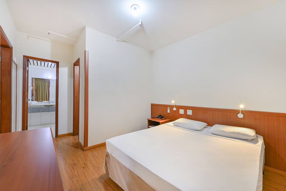 A hotel room with a wooden bed, a wooden nightstand, a telephone, and a mirror.