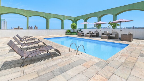 Un área de piscina en la azotea con sillones y sombrillas, rodeada por una estructura arqueada de vegetación.
