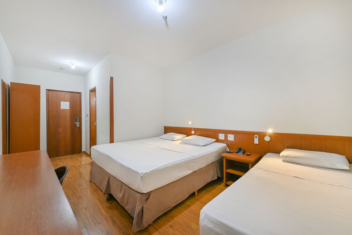 A hotel room with two single beds, a wooden desk, a nightstand with a lamp, and a door.