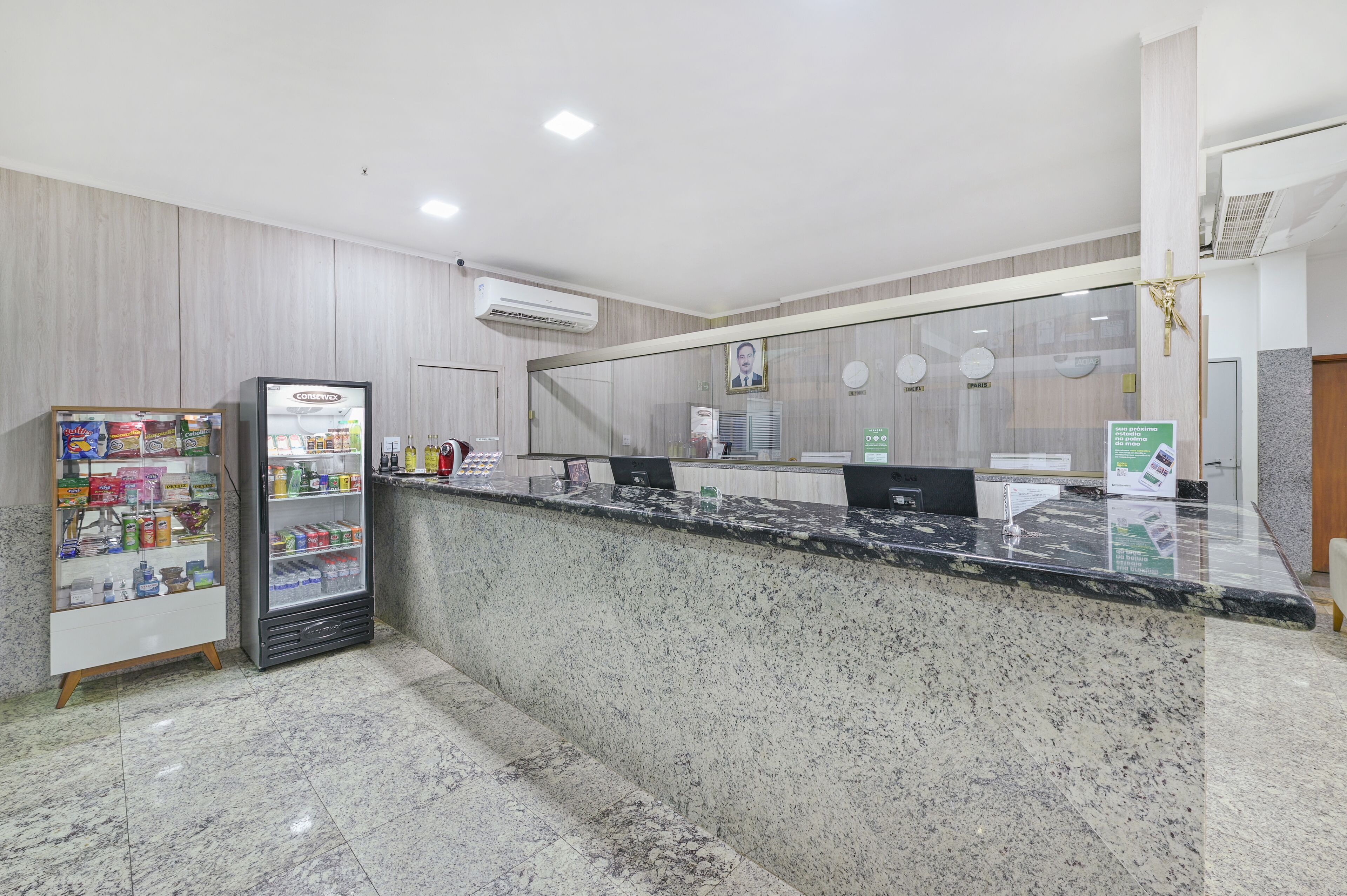 Una recepción con mostrador de mármol, vitrina refrigerada y un pequeño mostrador con diversos artículos.