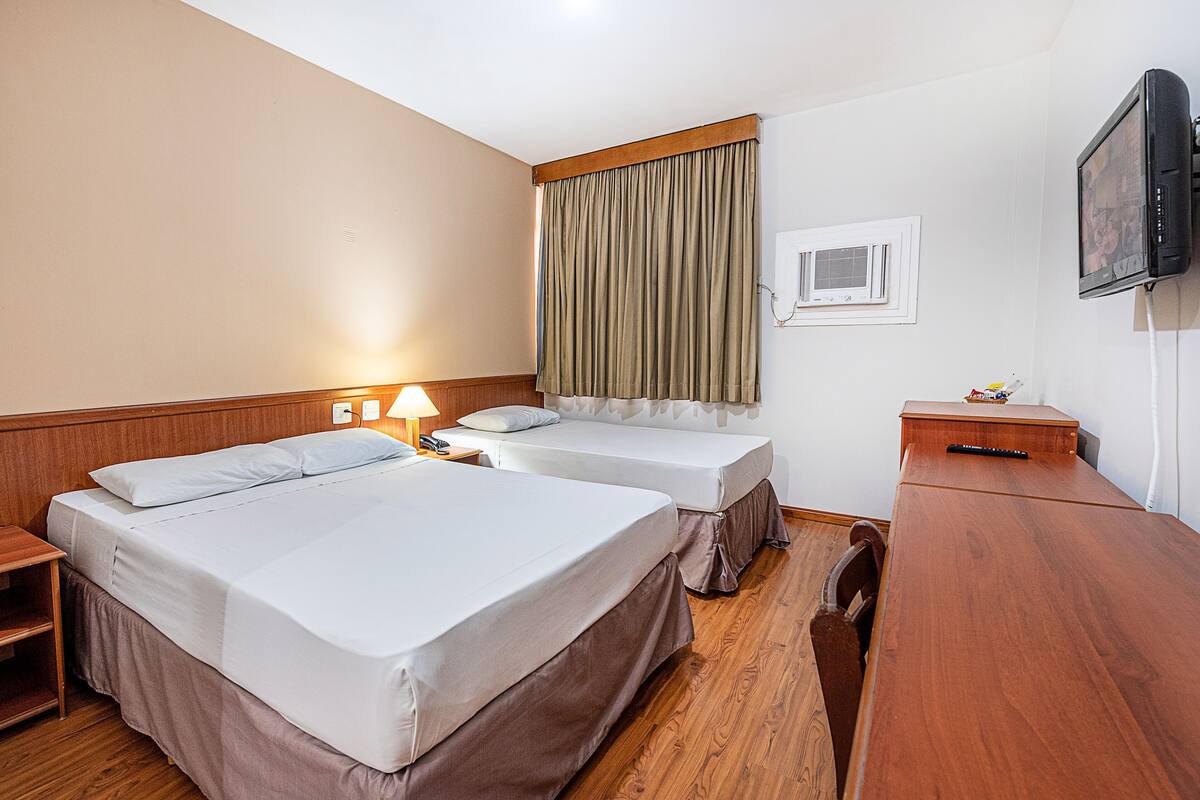 A hotel room with two beds, a wooden desk, a television, and a window with curtains.