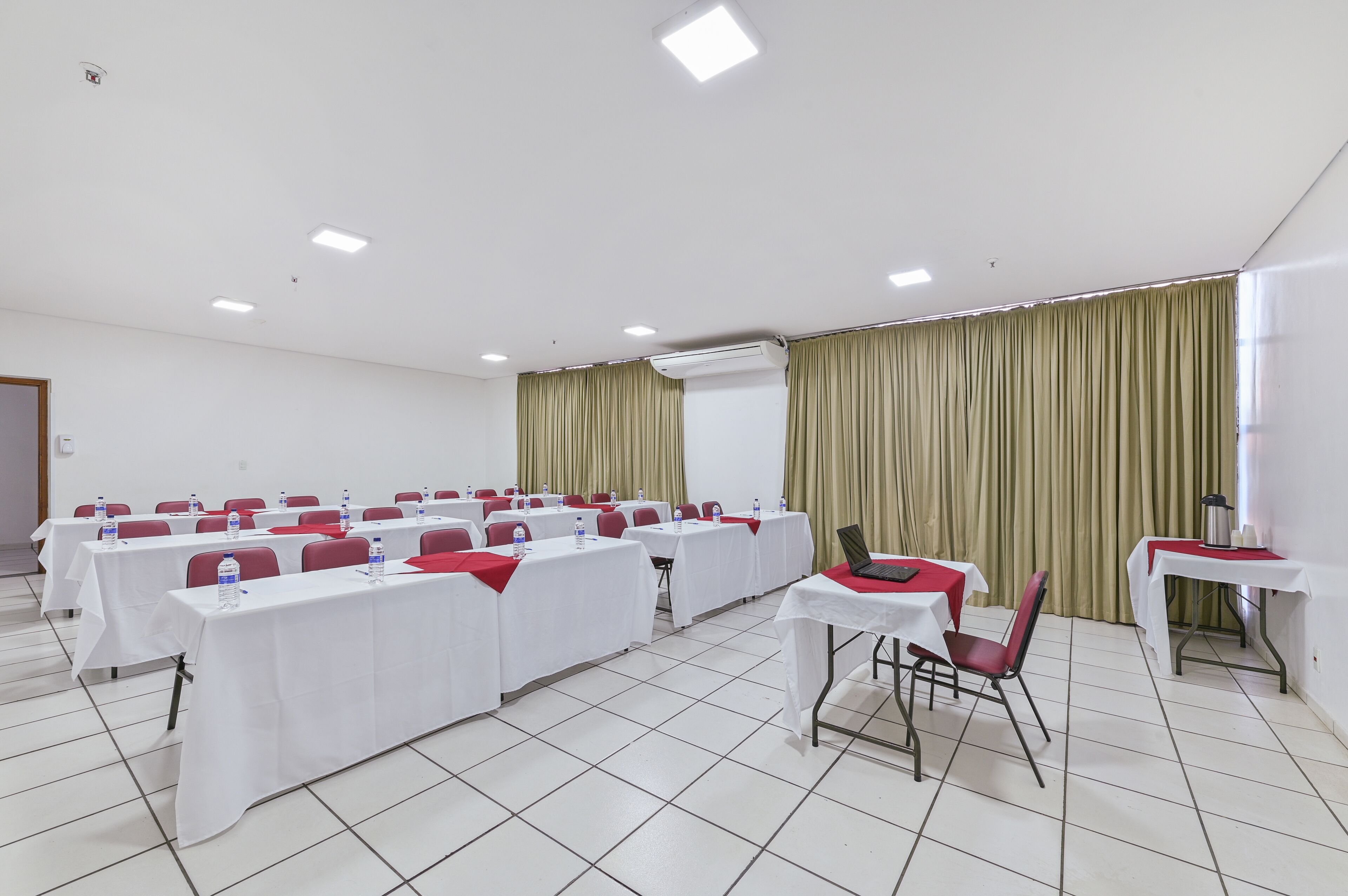 A conference room with tables and chairs, a white ceiling, and a window with curtains.
