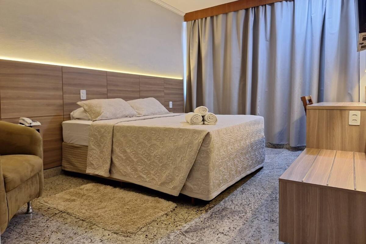 A hotel room with a bed, a desk, a chair, and a large window with curtains.