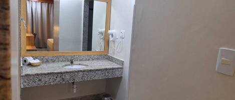 A bathroom with a granite countertop sink, a mirror with a wooden frame, a hairdryer, and a trash can.