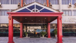 A hotel entrance with a red canopy, glass doors, and a reflection of a vehicle. - Hotel Nacional Inn Ribeirão Preto (Ribeirão Preto)