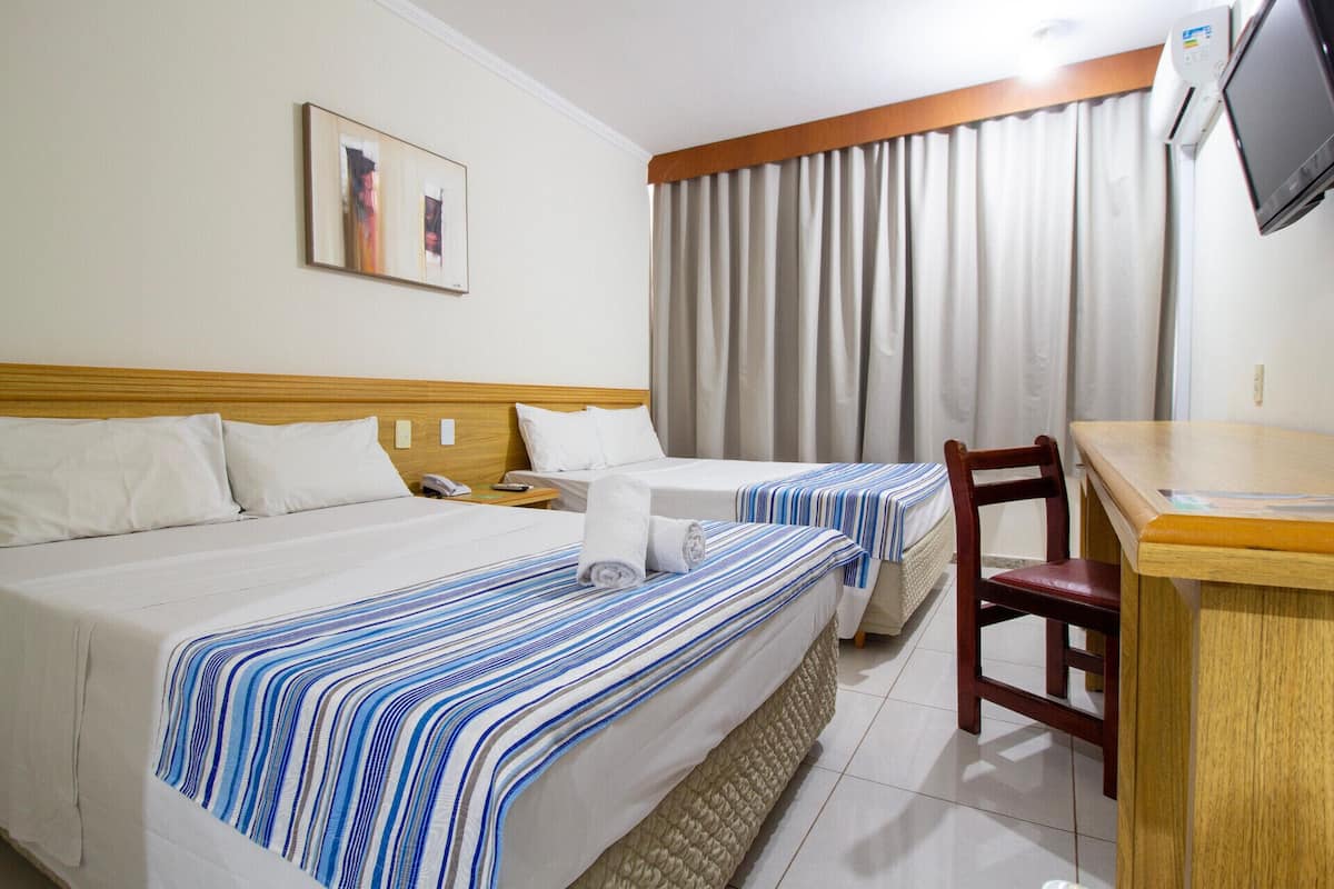 A hotel room with two beds, a desk, a chair, a television, and a window with curtains.