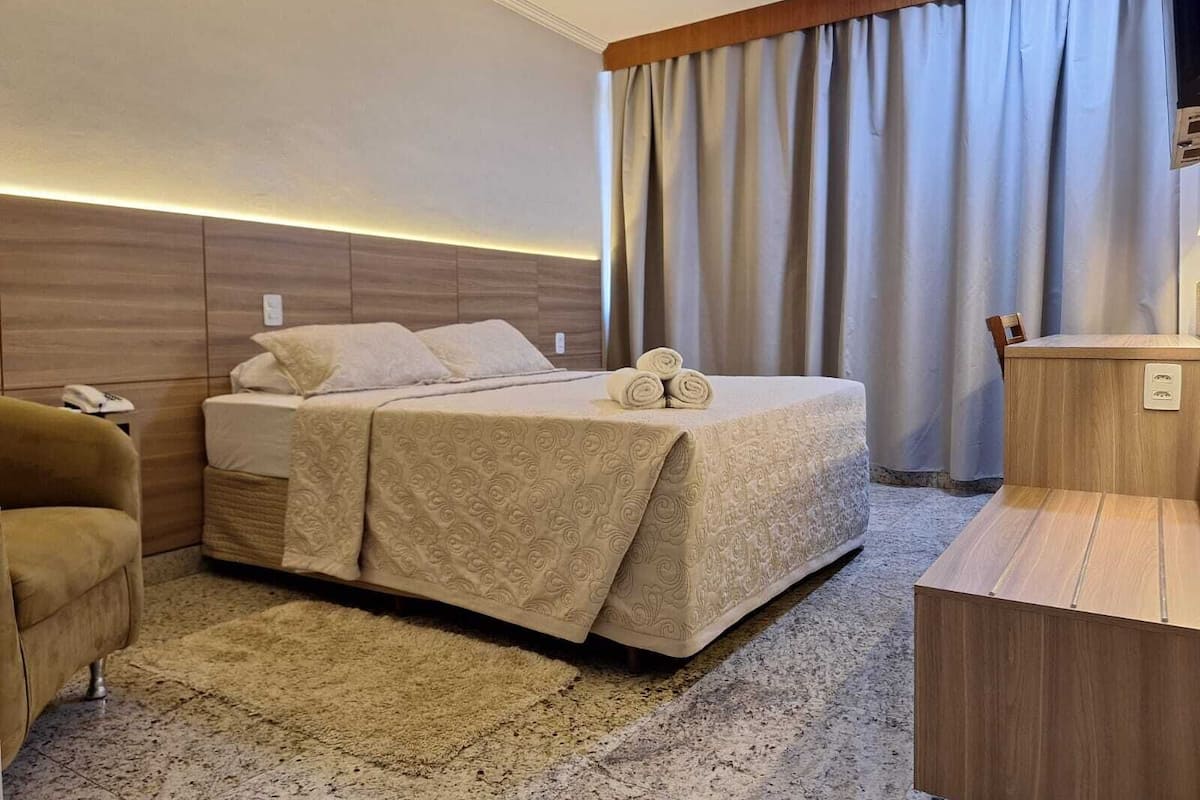 A hotel room with a bed, a desk, a chair, and a large window with curtains.