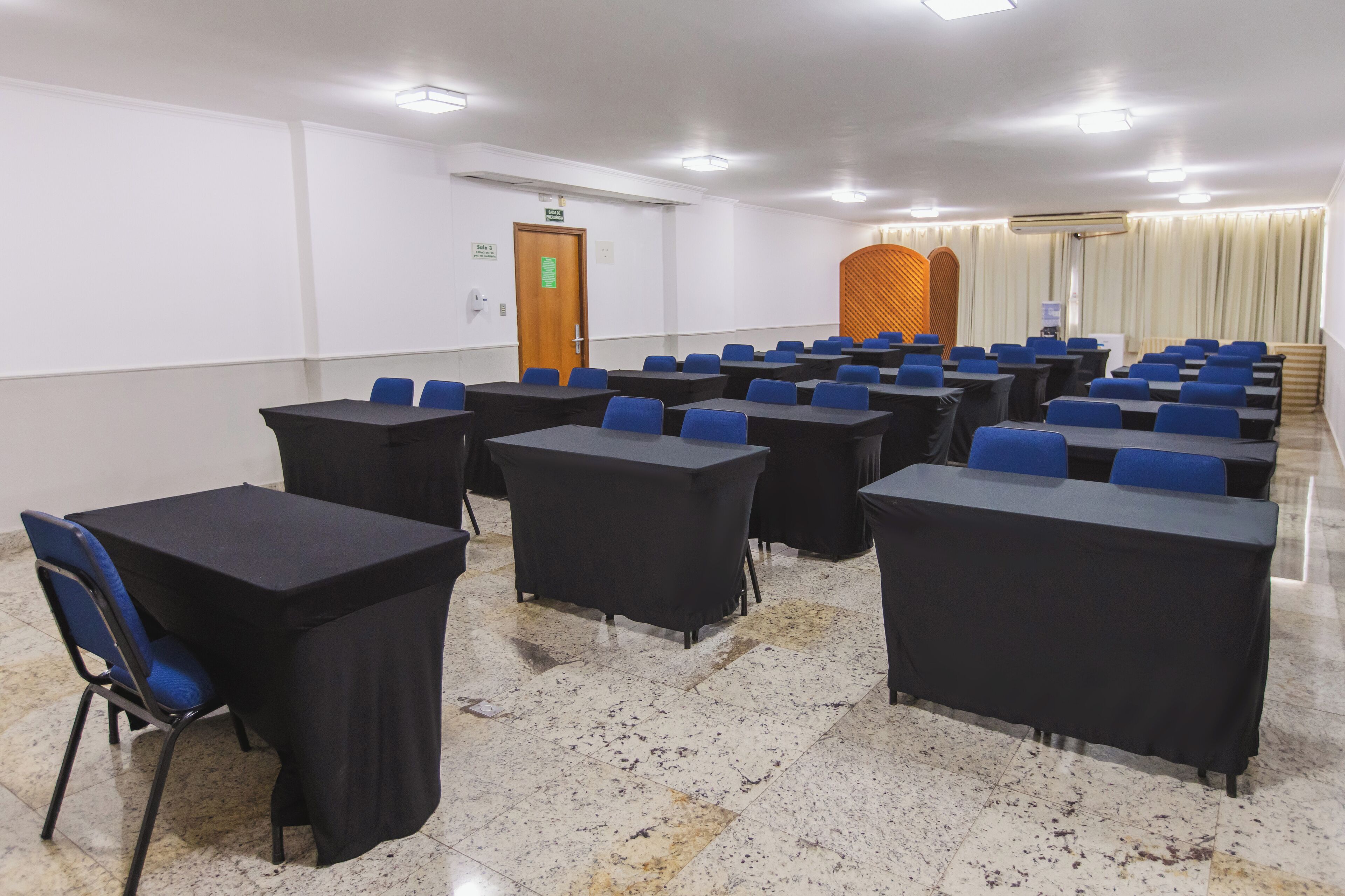 A conference room with multiple tables and chairs, a door with a sign, and an air conditioning unit on the wall.