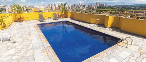 A rooftop pool with a city view, stone tiles, and potted plants.