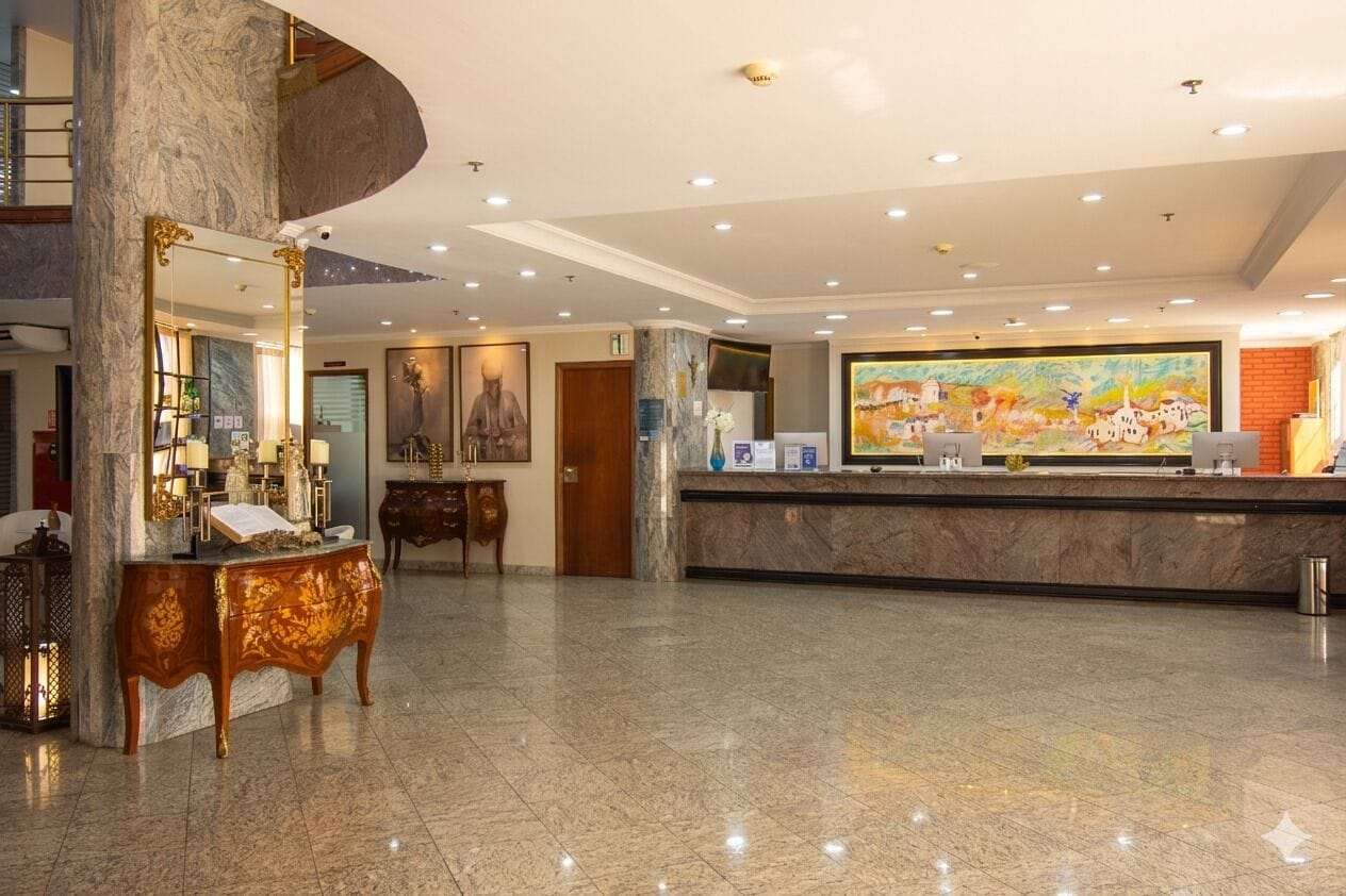 A hotel lobby with a marble reception desk, a large painting, and a spiral staircase.