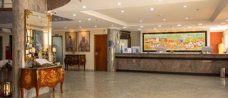 A hotel lobby with a marble reception desk, a large painting, and a spiral staircase.