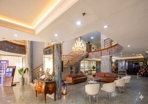 A spacious lobby with a marble floor, a grand staircase, and a chandelier.