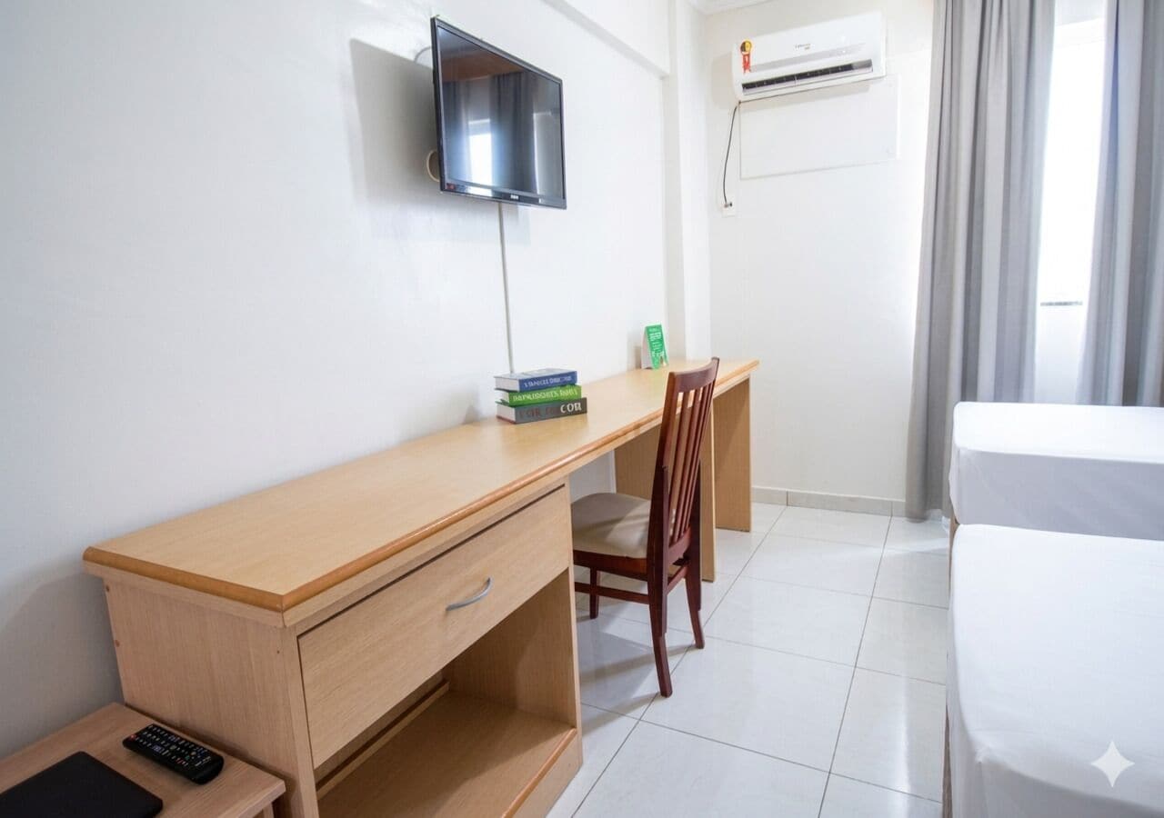 Ett hotellrum med ett skrivbord i trä, en tv som är monterad på väggen, en stol, en säng och en luftkonditioneringsanläggning.