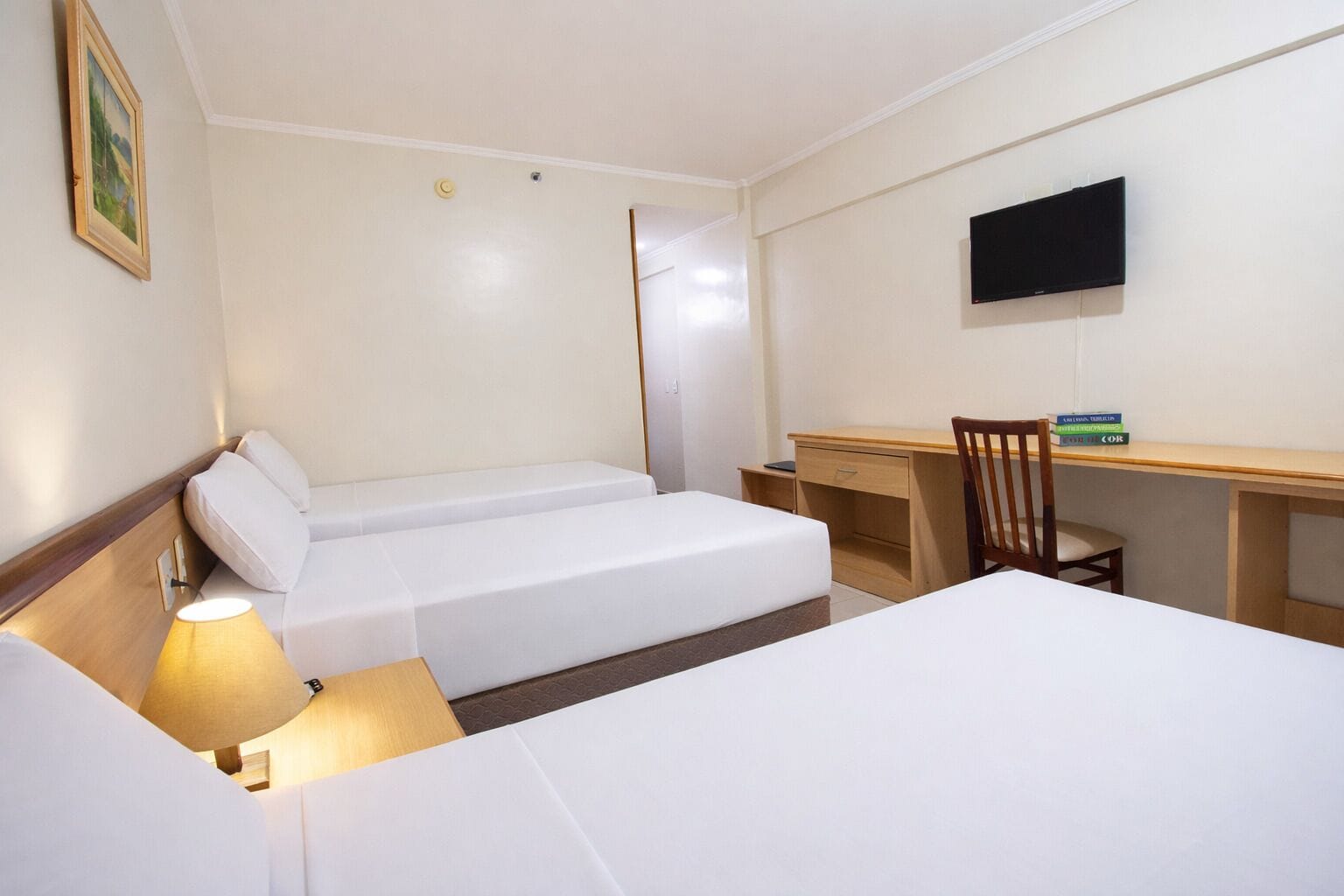 A hotel room with two beds, a desk, a chair, a TV, and a lamp.