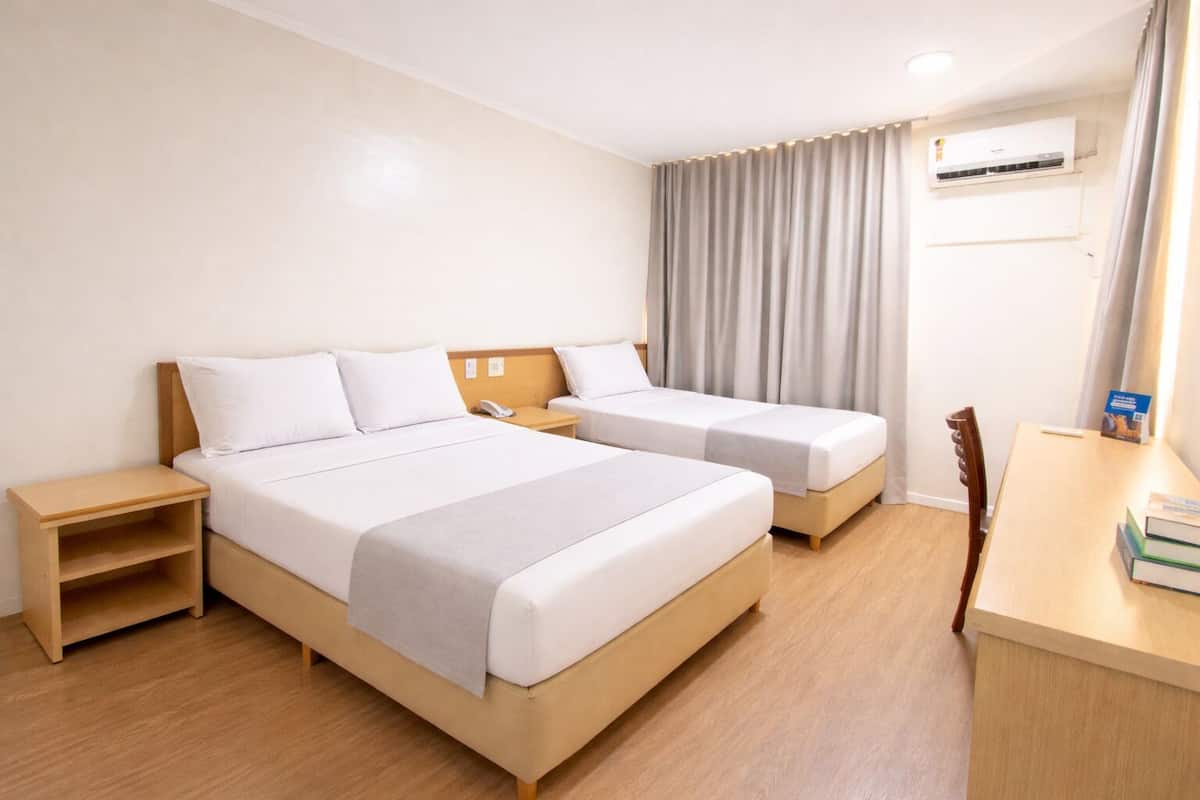 Ein Hotelzimmer mit zwei Betten, einem Schreibtisch, einem Sessel, einem Nachttisch, einer Klimaanlage und einem Vorhang.