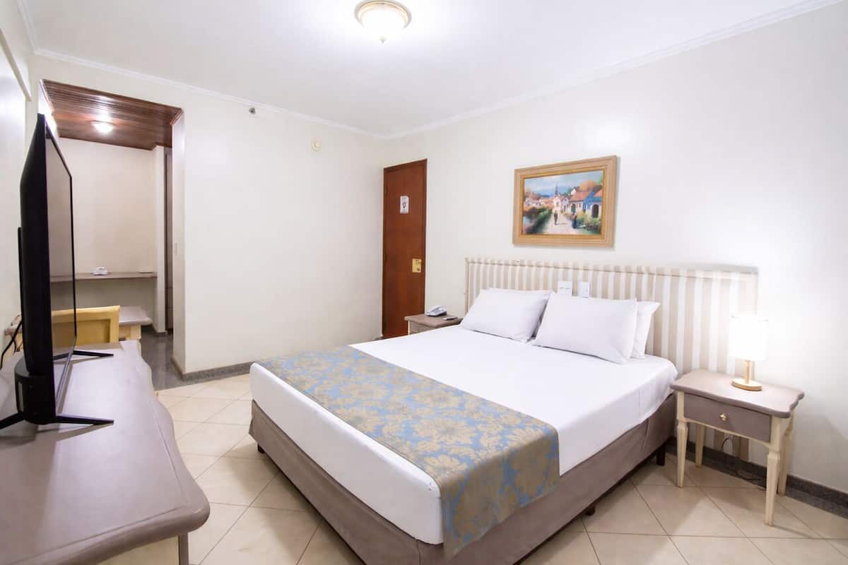 Ein Hotelzimmer mit Bett, Nachttisch, Lampe und einem Bild an der Wand.