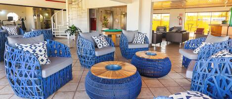 A lobby with wicker furniture, including sofas and round tables, and a staircase in the background.