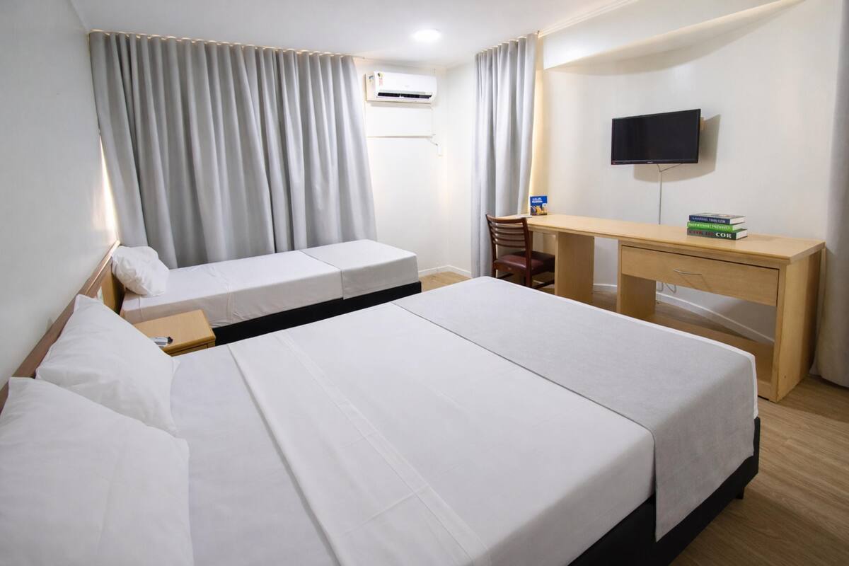 Ein Hotelzimmer mit zwei Betten, einem Schreibtisch, einem Stuhl, einem Flachbildfernseher und einer Klimaanlage.