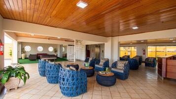 A spacious lobby with wooden ceiling, blue woven seating, and a green carpeted area.