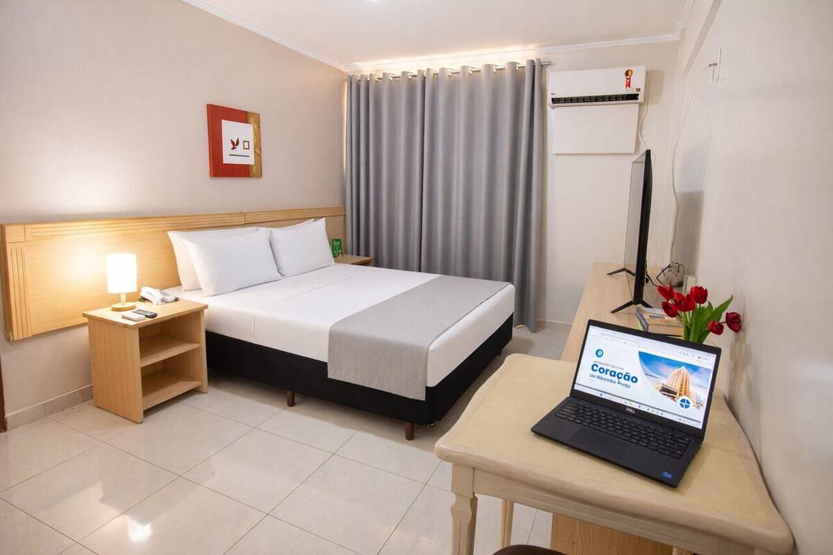 Ein Hotelzimmer mit Bett, Schreibtisch mit Laptop, Nachttisch mit Lampe und Klimaanlage.