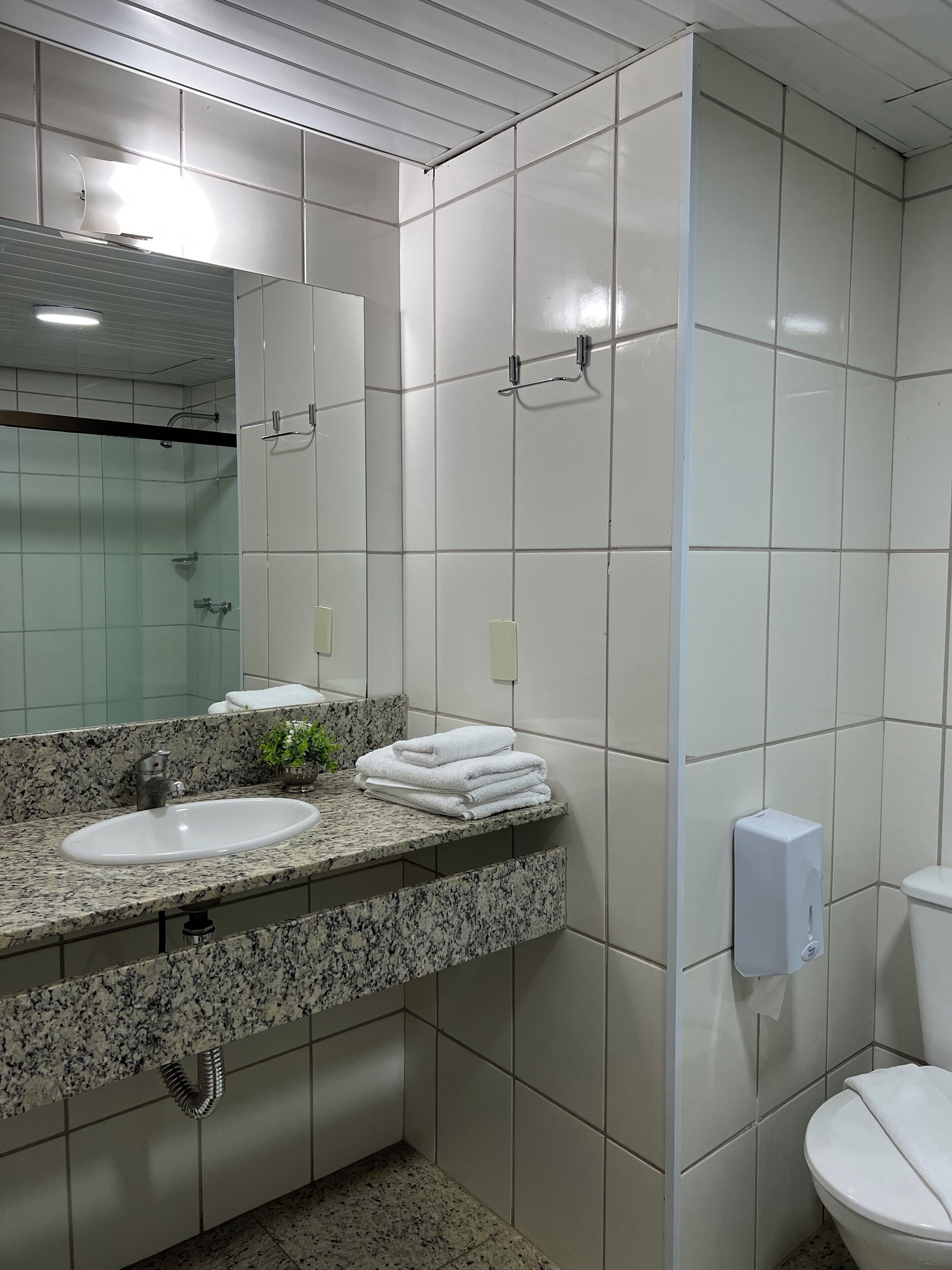 A bathroom with a granite countertop, a sink, a mirror, a toilet, and a hand dryer.