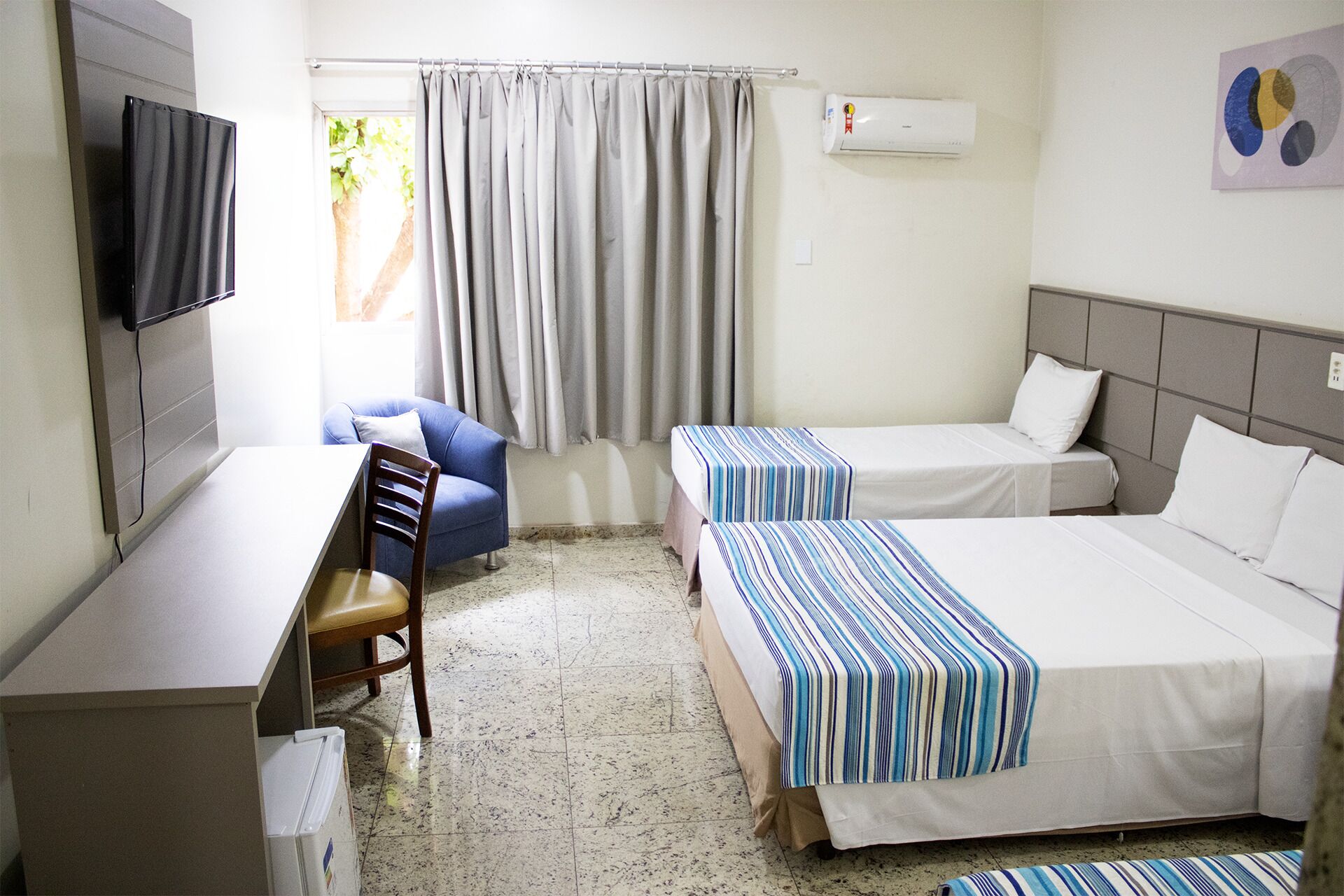 A hotel room with two beds, a desk, a chair, a TV, and a window with curtains.