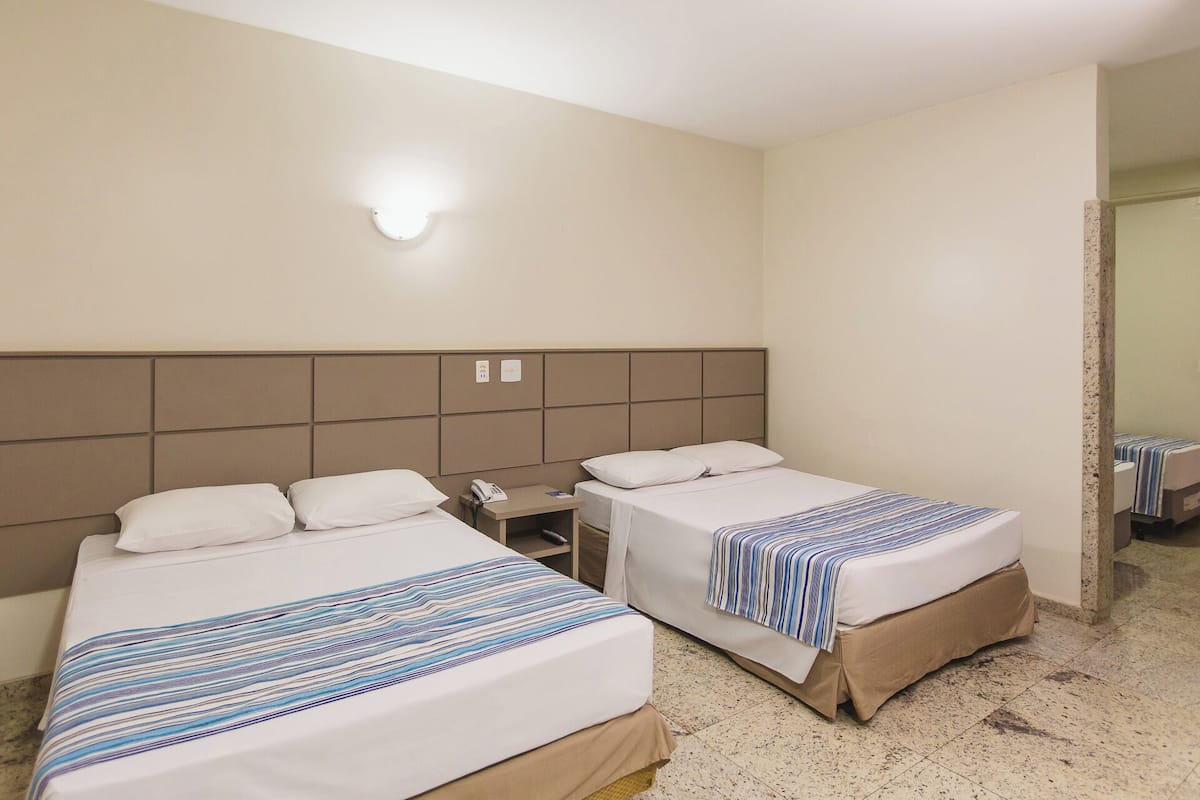 A hotel room with two beds, a bedside table with a phone, and a wall-mounted light.