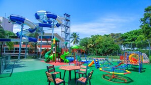Ein Spielplatz mit Rutschen, Schaukeln und einem eingezäunten Bereich mit Tischen und Stühlen.