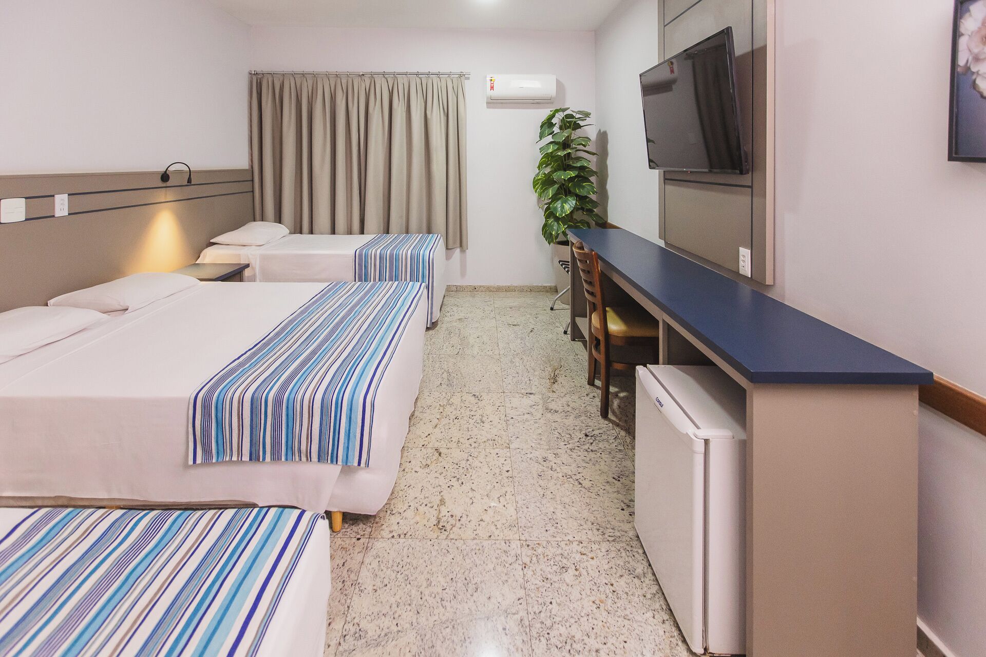 Ein Hotelzimmer mit zwei Betten, einem Schreibtisch, einem Fernseher und einer Pflanze.