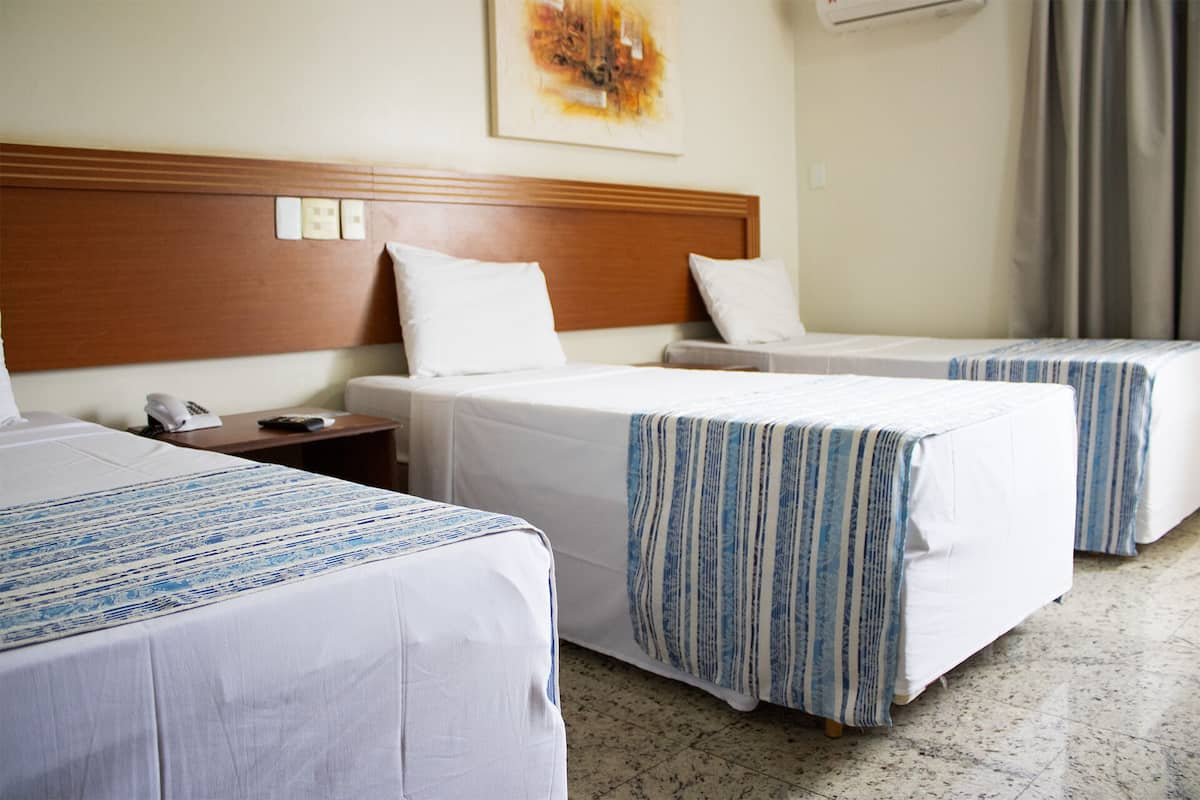 A hotel room with two beds, a wooden headboard, a bedside table with a phone, and a painting on the wall.