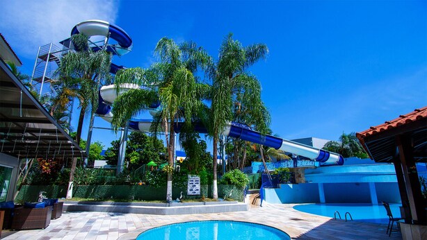 A pool area with a water slide, palm trees, and a tiled deck. - Hotel Vilage Inn Ribeirão Preto & Convenções By Nacional Inn (Ribeirão Preto)