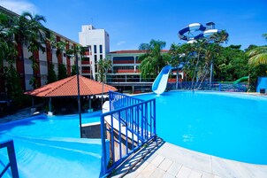 Una piscina con tobogán de agua, rodeada de palmeras y un edificio de techo rojo.