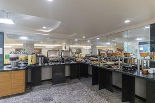 Disposição de buffet com diversas estações de comida, piso de mármore e design moderno no teto.