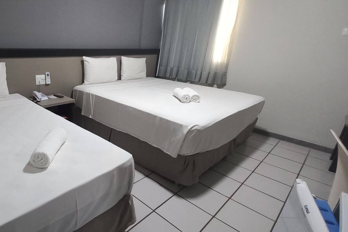 A hotel room with two single beds, a nightstand with a phone, and a window with curtains.
