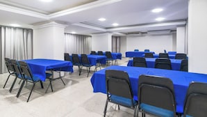 Une salle de conférence dotée de plusieurs tables et chaises, de murs blancs et d’un éclairage au plafond.