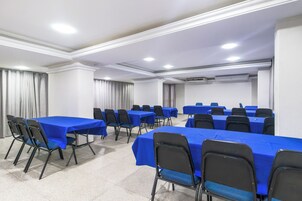 Uma sala de conferências com várias mesas e cadeiras, paredes brancas e luminárias no teto.
