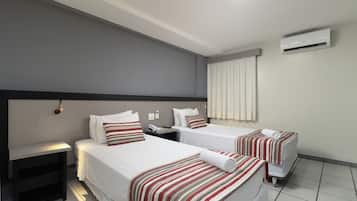 A hotel room with two beds, a bedside table, a phone, and an air conditioning unit.