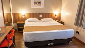 Quarto de hotel com cama, mesas de cabeceira, escrivaninha e uma cadeira.