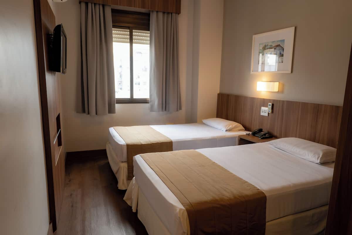 Une chambre d’hôtel avec deux lits, une télévision, une lampe de chevet, un téléphone et une fenêtre avec des rideaux.