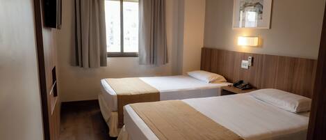 A hotel room with two beds, a TV, a bedside lamp, a phone, and a window with curtains.