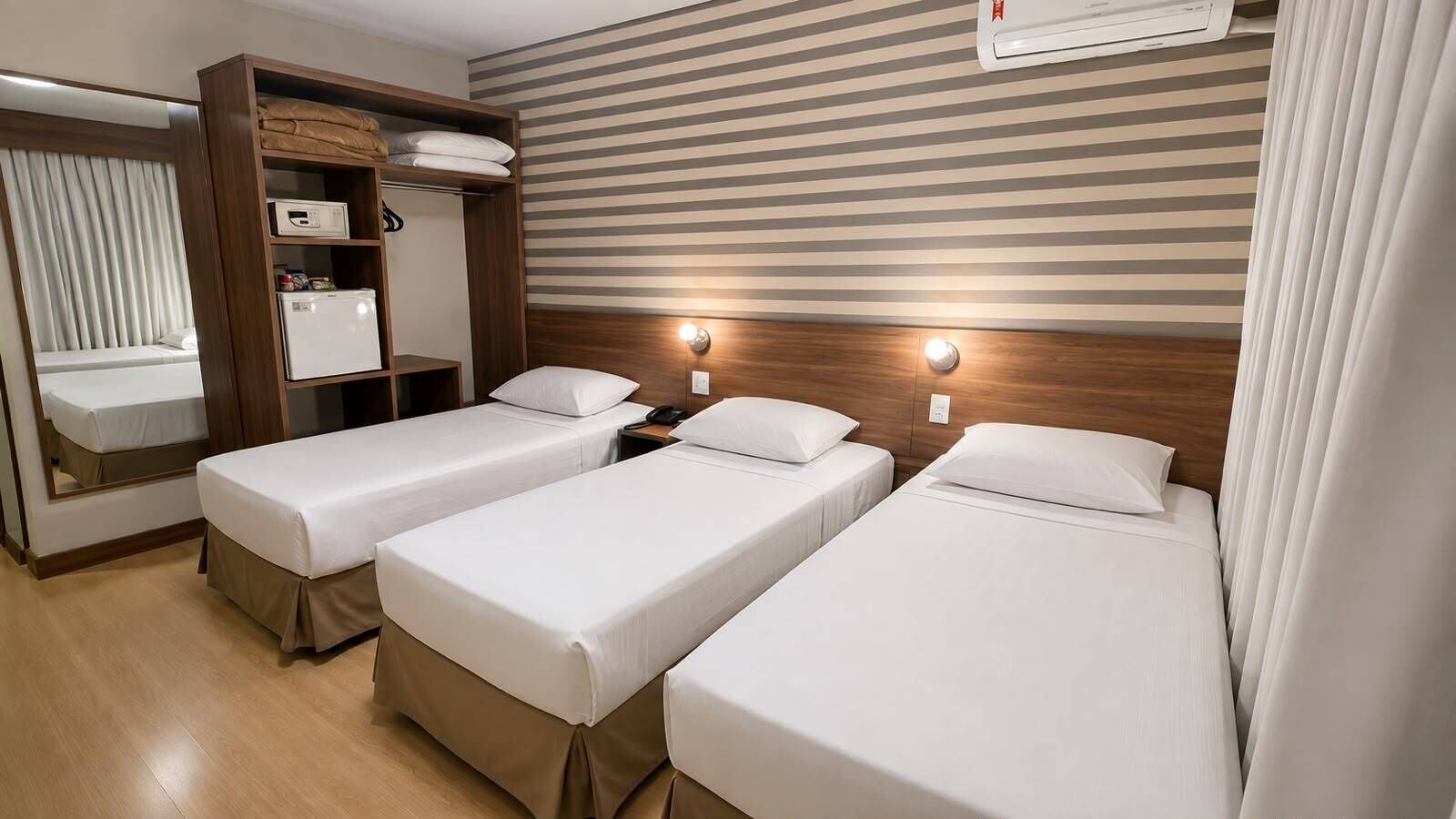 A hotel room with two single beds, a wardrobe, a mirror, and a striped wall.