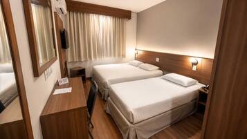 A compact hotel room with two beds, a desk, a mirror, and a window with curtains.